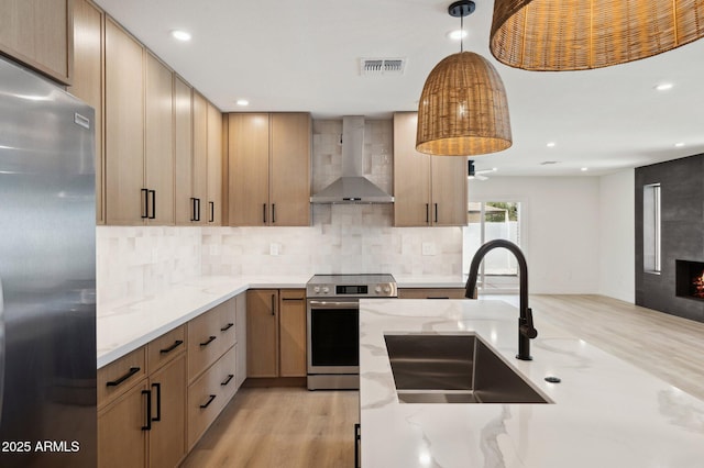 kitchen with stainless steel appliances, wall chimney exhaust hood, a sink, light wood-style floors, and recessed lighting