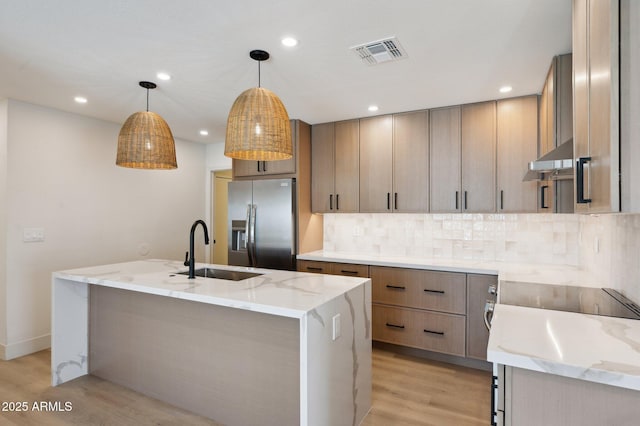 kitchen featuring stainless steel fridge, a sink, light wood-style flooring, light stone countertops, and backsplash