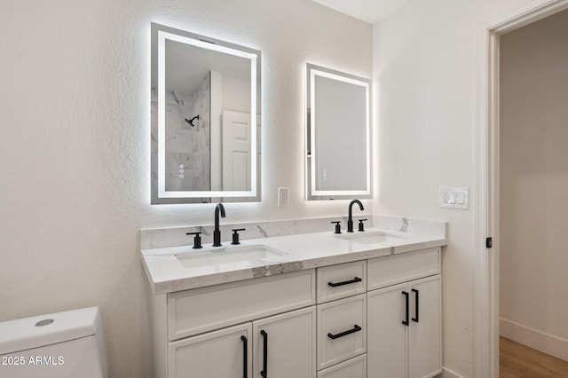 bathroom with toilet, double vanity, a shower, and wood finished floors