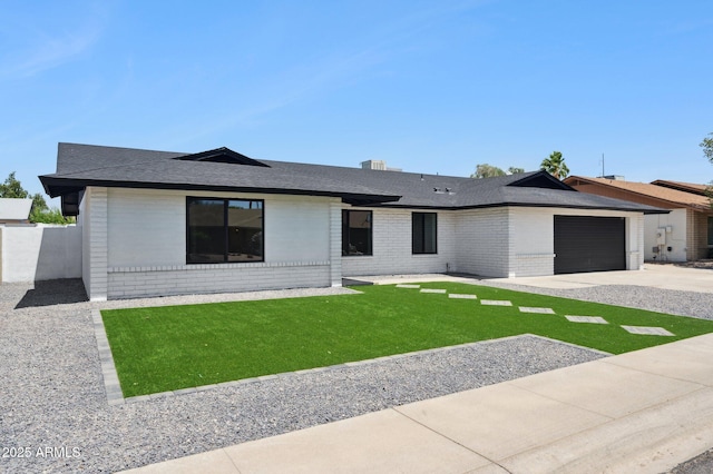 ranch-style home featuring brick siding, a garage, concrete driveway, a front yard, and a shingled roof