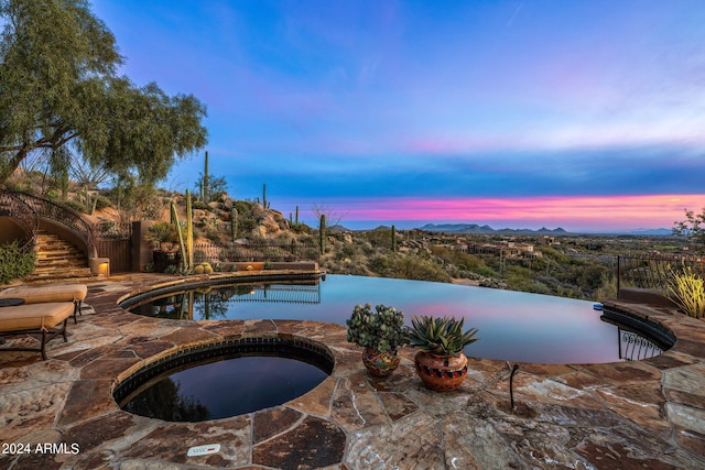 pool at dusk with an in ground hot tub and a patio area