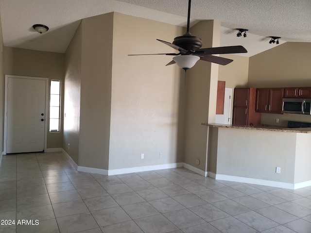 unfurnished living room with a textured ceiling, light tile patterned floors, ceiling fan, and high vaulted ceiling