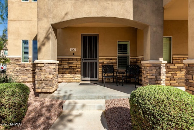 property entrance with stone siding, covered porch, and stucco siding