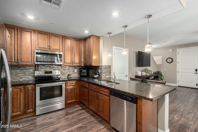 kitchen with visible vents, brown cabinetry, a peninsula, stainless steel appliances, and a sink