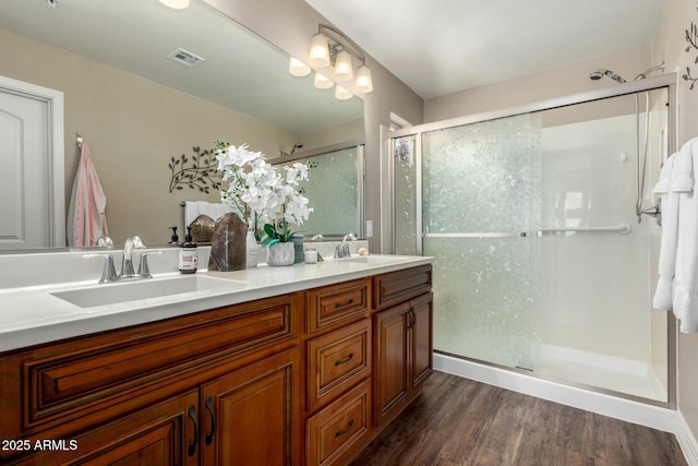 full bath with double vanity, a stall shower, visible vents, wood finished floors, and a sink