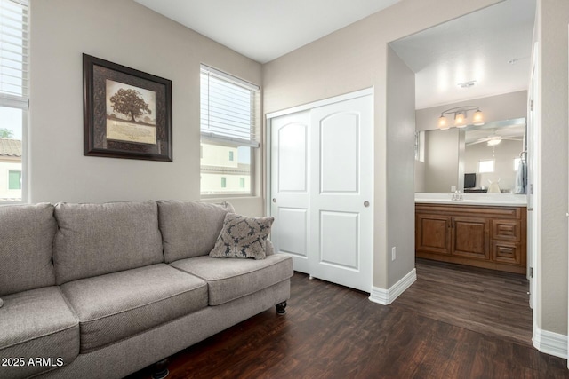 living area with baseboards, dark wood-style flooring, and a healthy amount of sunlight