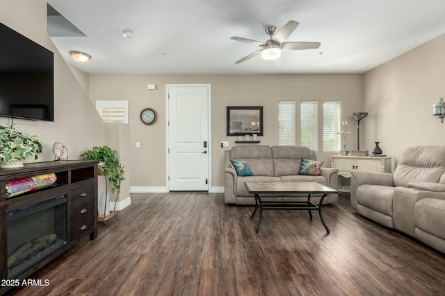 living room with ceiling fan, baseboards, dark wood-style flooring, and a glass covered fireplace