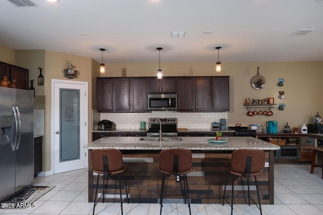 18309 N Crestview Ln, Maricopa, AZ 85138 - kitchen featuring appliances with stainless steel finishes, decorative backsplash, dark brown cabinets, a sink, and a kitchen bar