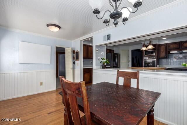 315 N 4th St, Tombstone, AZ 85638 - dining room with crown molding, a chandelier, visible vents, a wainscoted wall, and light wood-type flooring