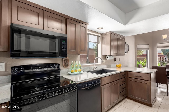 kitchen with a peninsula, a sink, light countertops, a wealth of natural light, and black appliances