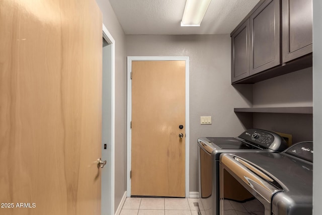 washroom with a textured ceiling, light tile patterned flooring, baseboards, cabinet space, and washing machine and clothes dryer