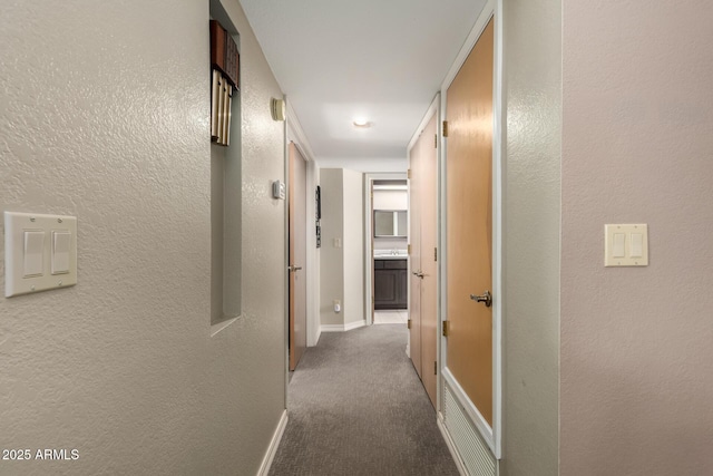 corridor featuring carpet, a textured wall, and baseboards