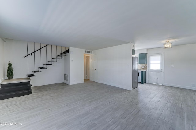 unfurnished living room featuring light wood-style floors, visible vents, and stairs