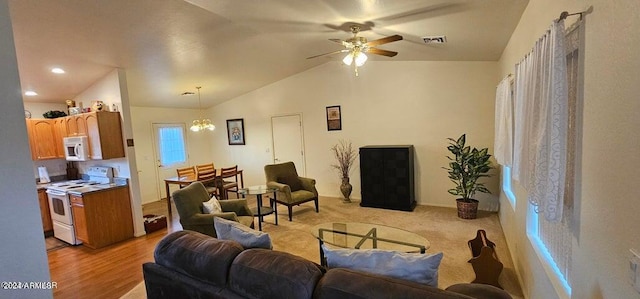 carpeted living room with ceiling fan with notable chandelier and vaulted ceiling