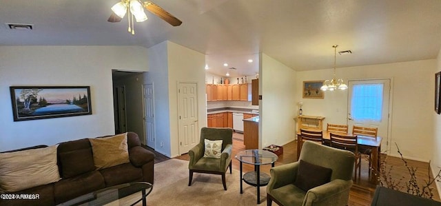 living room with ceiling fan with notable chandelier, vaulted ceiling, and light hardwood / wood-style flooring