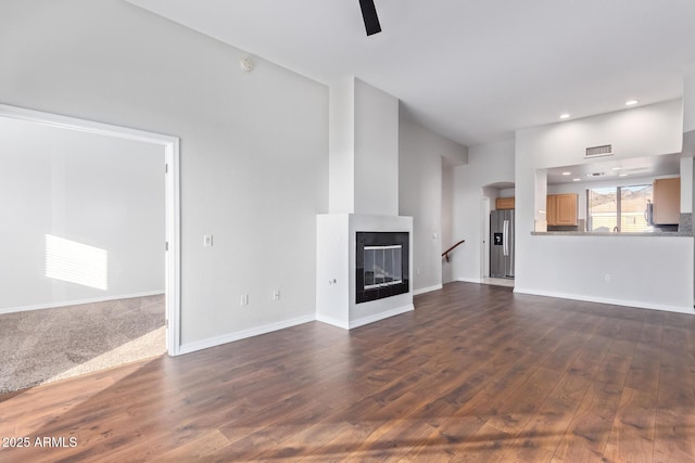 unfurnished living room with ceiling fan, dark hardwood / wood-style flooring, and a multi sided fireplace