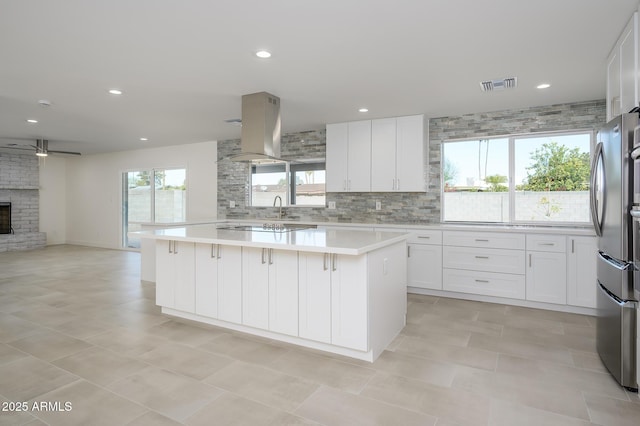 kitchen featuring island exhaust hood, stainless steel refrigerator, white cabinets, and a kitchen island