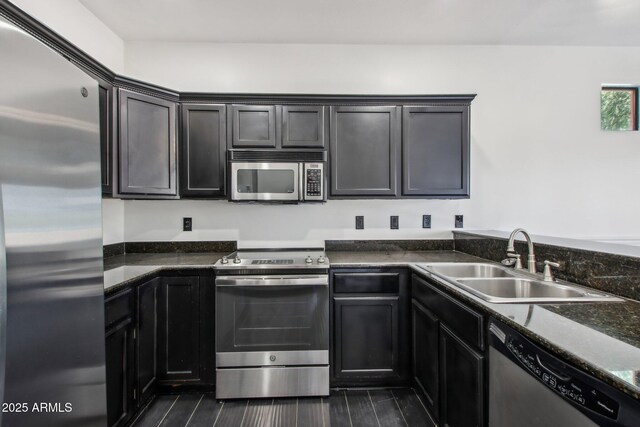 kitchen with appliances with stainless steel finishes, a sink, and dark stone counters