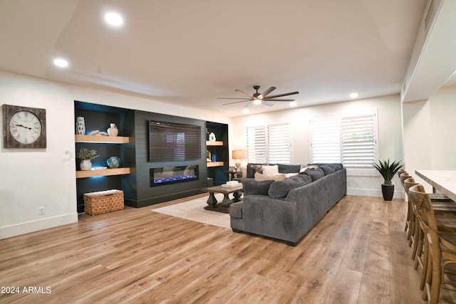 living room with built in shelves, ceiling fan, a fireplace, and light hardwood / wood-style floors