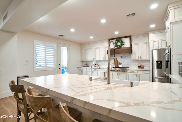 kitchen with light stone counters, stainless steel fridge with ice dispenser, backsplash, a kitchen bar, and white cabinets