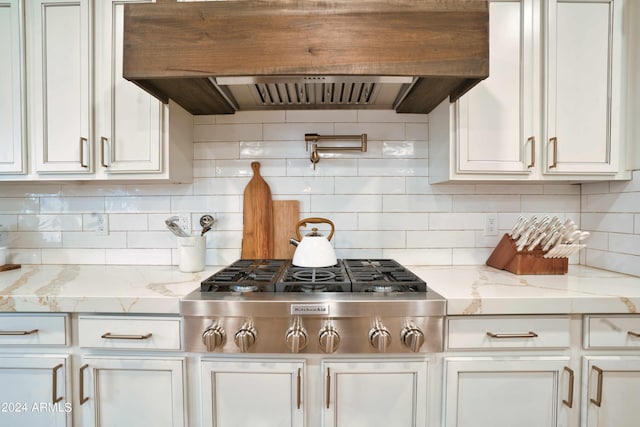 kitchen featuring stainless steel gas stovetop, white cabinets, decorative backsplash, light stone countertops, and range hood