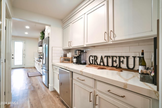 kitchen featuring tasteful backsplash, light hardwood / wood-style floors, light stone counters, white cabinetry, and stainless steel refrigerator