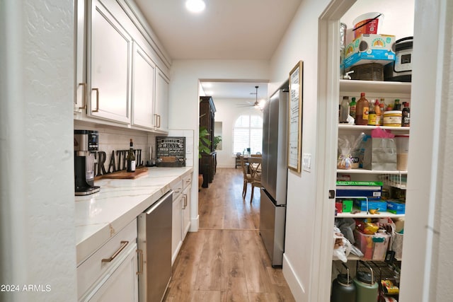 bar with light stone counters, light hardwood / wood-style flooring, white cabinets, and ceiling fan