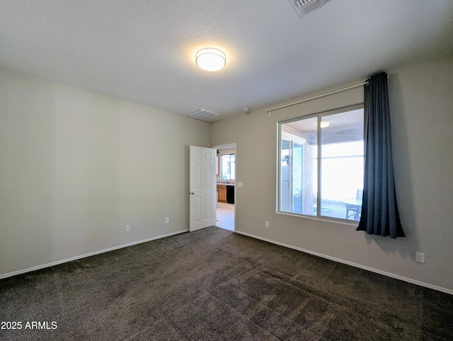 spare room featuring dark carpet and a textured ceiling