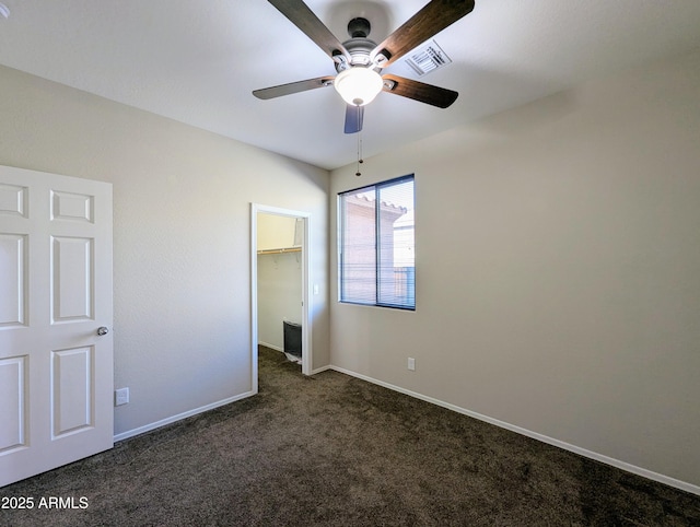 unfurnished bedroom featuring a spacious closet, a closet, ceiling fan, and dark colored carpet