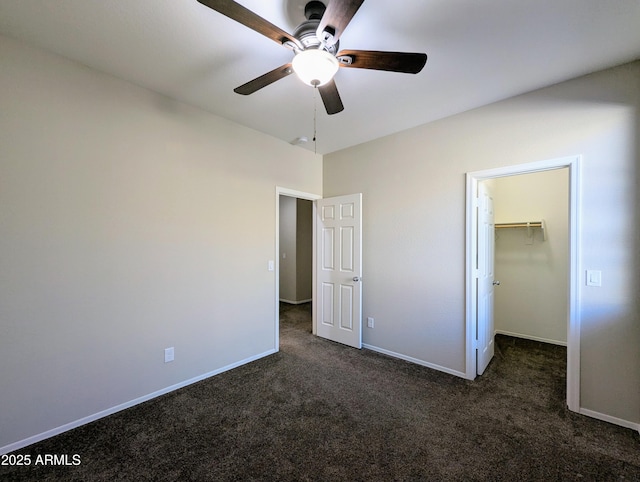 unfurnished bedroom with a spacious closet, a closet, ceiling fan, and dark colored carpet