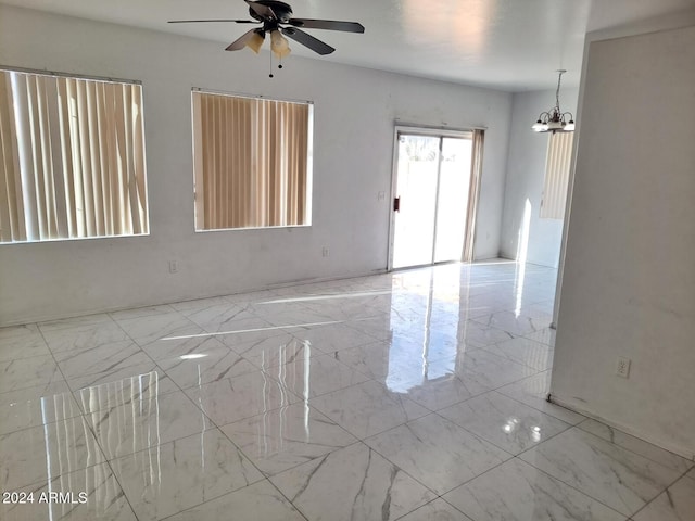 spare room featuring ceiling fan with notable chandelier