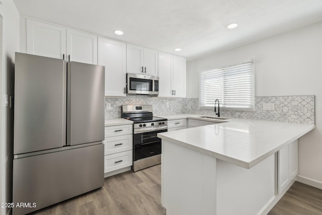 kitchen featuring white cabinets, appliances with stainless steel finishes, a peninsula, light wood-type flooring, and a sink