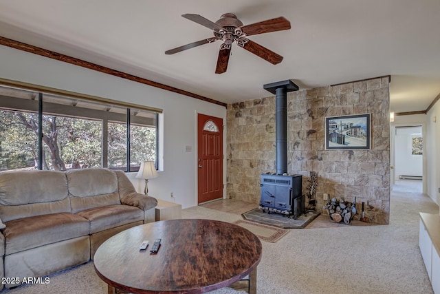 living area with crown molding, ceiling fan, carpet flooring, a wood stove, and a baseboard radiator