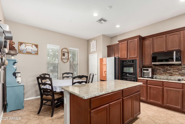 kitchen featuring tasteful backsplash, visible vents, a center island, light stone counters, and black appliances