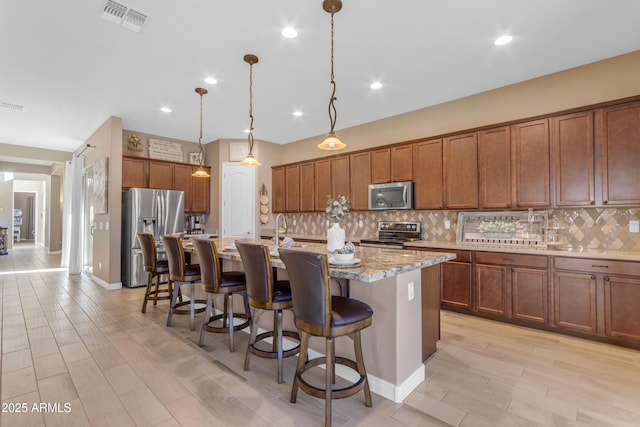 10650 E Palladium Dr, Mesa, AZ 85212 - kitchen featuring appliances with stainless steel finishes, backsplash, brown cabinetry, a breakfast bar, and a kitchen island with sink