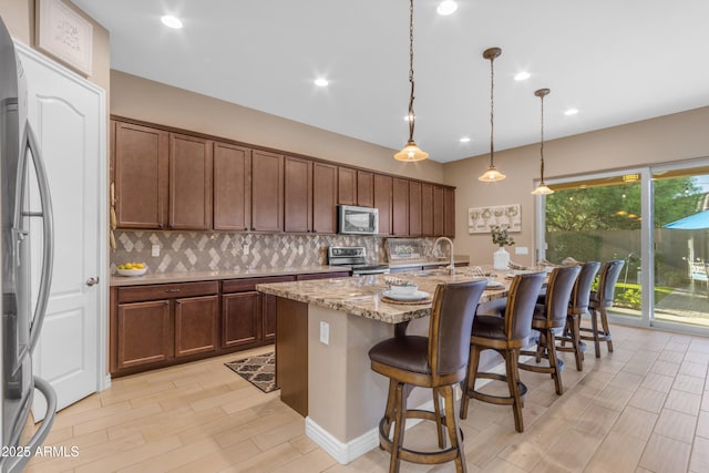 10650 E Palladium Dr, Mesa, AZ 85212 - kitchen featuring stainless steel appliances, tasteful backsplash, an island with sink, a breakfast bar, and light stone countertops