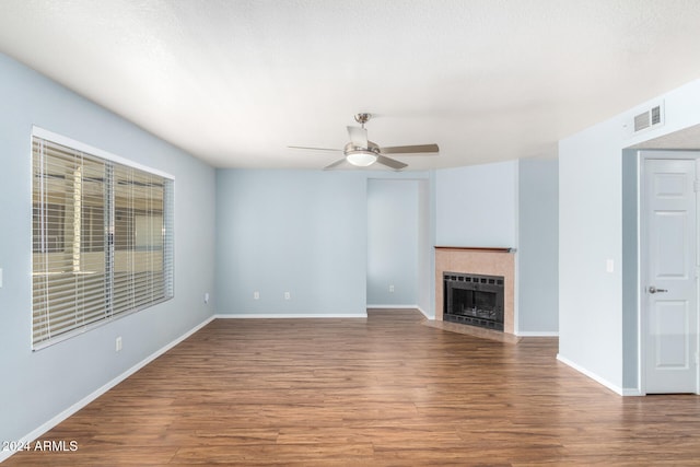 unfurnished living room featuring ceiling fan, a tile fireplace, and dark hardwood / wood-style floors