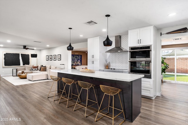 8341 E Hubbell St, Scottsdale, AZ 85257 - kitchen featuring wall chimney range hood, stainless steel double oven, wood finished floors, a kitchen island, and recessed lighting