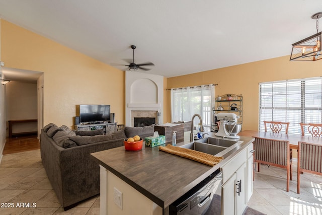 kitchen featuring a ceiling fan, a tiled fireplace, a center island with sink, dishwasher, and a sink