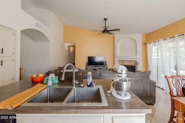 kitchen with a ceiling fan, open floor plan, white cabinets, a tile fireplace, and a sink