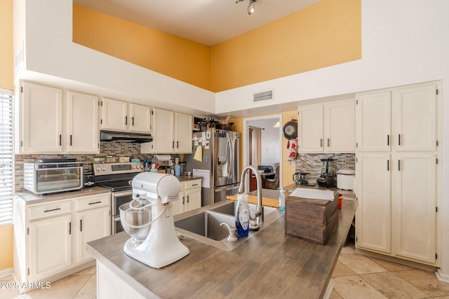 kitchen featuring a towering ceiling, stainless steel appliances, a toaster, under cabinet range hood, and visible vents