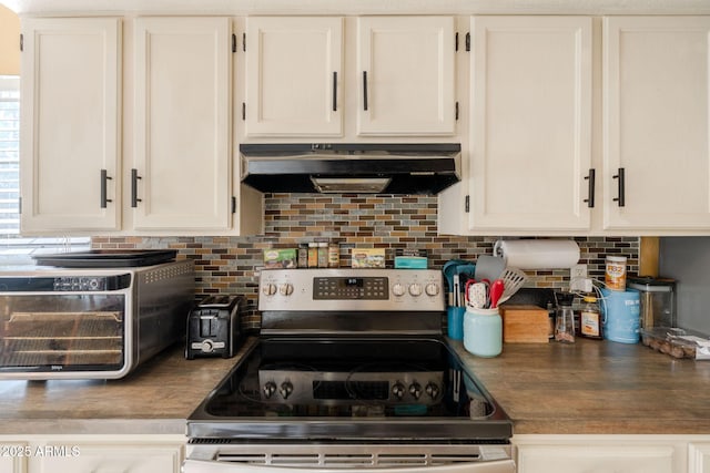kitchen featuring decorative backsplash, electric range, a toaster, dark countertops, and under cabinet range hood