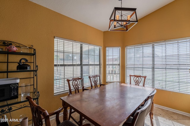 tiled dining space with baseboards, a textured wall, vaulted ceiling, and a chandelier