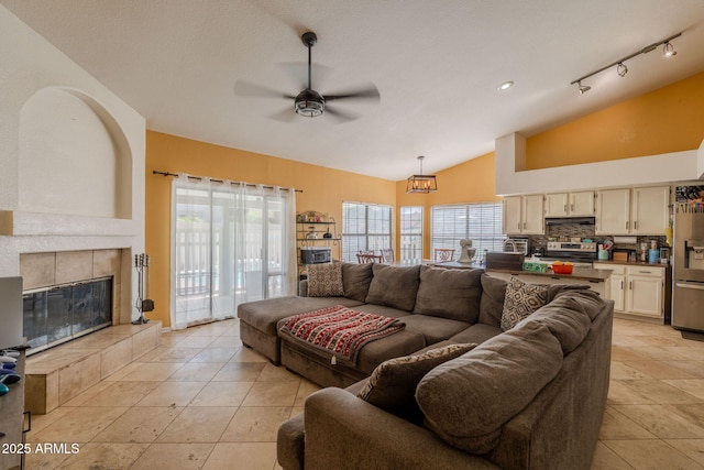 living room featuring a ceiling fan, lofted ceiling, light tile patterned flooring, and a fireplace