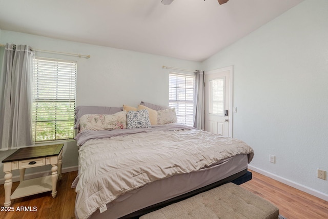 bedroom with baseboards, lofted ceiling, multiple windows, and wood finished floors