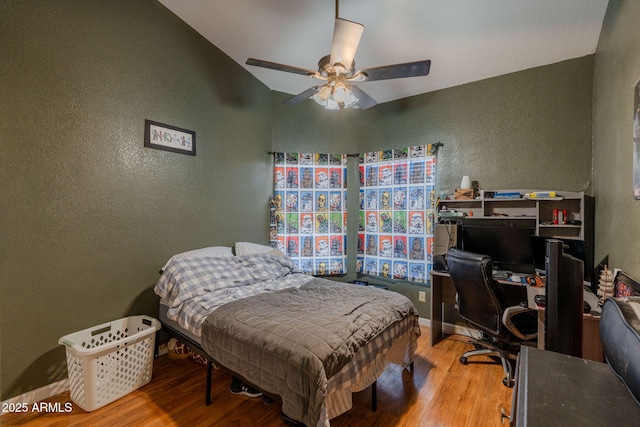 bedroom featuring baseboards, a textured wall, a ceiling fan, and wood finished floors
