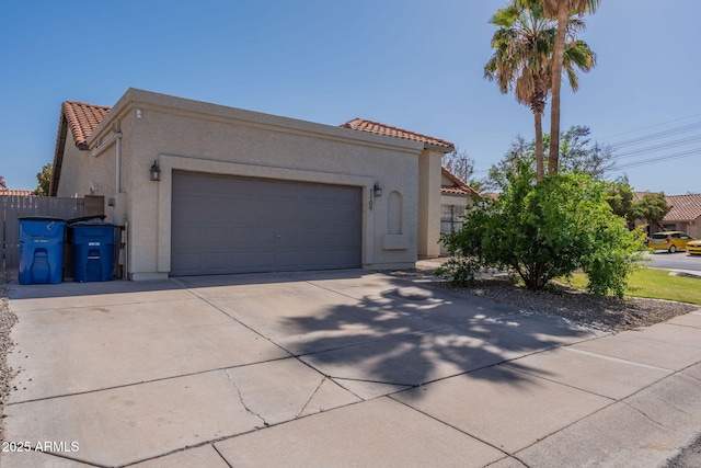 view of front of house featuring a garage, fence, stucco siding, a tiled roof, and driveway