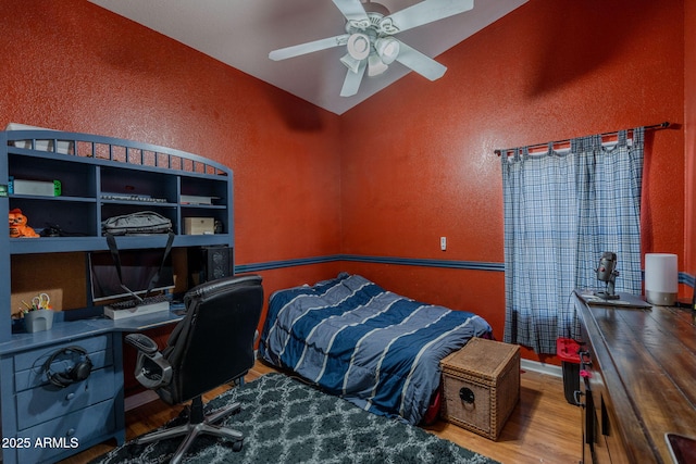 bedroom with a textured wall, a ceiling fan, wood finished floors, and lofted ceiling