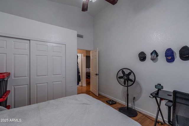 bedroom featuring high vaulted ceiling, baseboards, wood finished floors, visible vents, and a closet