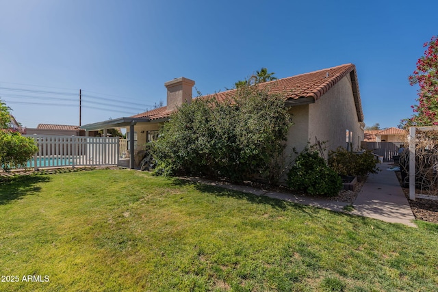 exterior space featuring fence, stucco siding, a chimney, a lawn, and a tile roof